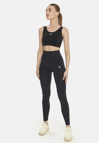 Črn športni crop top in visoko pasne legice iz elastične tkanine, z majhnim logotipom na prsih in stegnu.