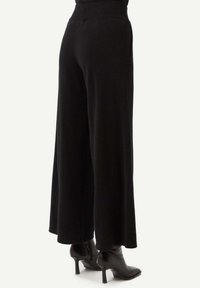 Svarta breda byxor gjorda av mjukt tyg. Midjebandet är elastiskt och har sidofickor. Bärs med svarta klackboots.