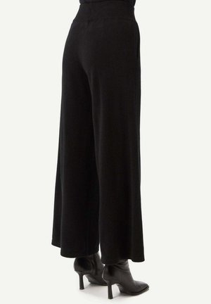 Schwarze, weite Hosen aus weichem Stoff. Der Bund ist elastisch und hat Seitentaschen. Dazu werden schwarze Stiefel mit Absatz getragen.