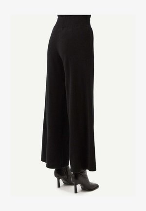 Schwarze, weite Hosen aus weichem Stoff. Der Bund ist elastisch und hat Seitentaschen. Dazu werden schwarze Stiefel mit Absatz getragen.