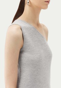 Grå utan ärmar topp gjord av ett mjukt, fint stickat material. Har en asymmetrisk design med en bred halsringning och subtil textur.