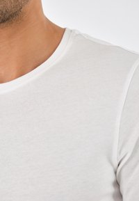 T-shirt bianco in cotone con colletto a girocollo, texture liscia e maniche corte, con una sottile cucitura decorativa lungo il colletto.