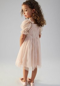 Das hellrosa Kleid verfügt über Puffärmel, einen taillierten Oberteil und einen weit ausgestellten, durchsichtigen Rock. Das Kleid hat eine strukturierte Oberfläche und dezente Akzente.