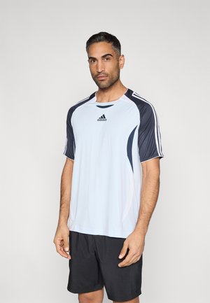 Αθλητική μπλούζα ανοιχτού γαλάζιου με σκούρες μπλε λεπτομέρειες και τρεις λευκές ρίγες στα μανίκια, συνδυασμένη με μαύρο σορτς. Ελαφρύ, κοντομάνικο σχέδιο.