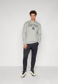 Szürke pulóver "NEW YORK" felirattal és tengerészkék részletekkel, sötétkék joggernadrággal és fehér sportcipővel párosítva. Az anyag puha és kényelmes megjelenésű.