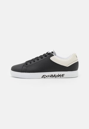 Black leather athletic shoe with white accents, rounded toe, lace-up front, and "EXCHANG" printed in black on the side. White rubber sole.