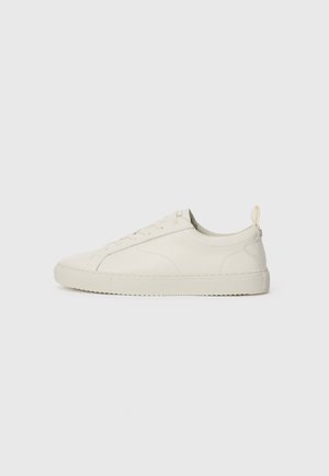 Light beige leather sneaker with a rounded toe, lace-up design, minimal stitching, and a textured rubber sole. Rear pull tab included.