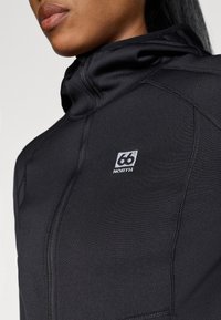 Casaco preto com fecho zip e gola alta, apresentando costuras planas e um pequeno logótipo bordado "66° NORTH" no peito. Textura suave.