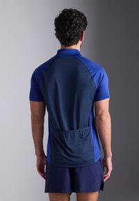 Αθλητική ανδρική μπλούζα σε μπλε αποχρώσεις, με κοντό μανίκι, λεία υφή και πίσω ελαστική τσέπη για αποθήκευση.