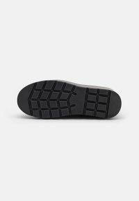 Suola di scarpa in gomma nera con un motivo testurizzato, caratterizzata da scanalature profonde e sezioni rialzate per una maggiore aderenza. Finitura liscia attorno ai bordi.