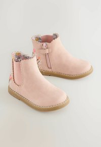 Cizme de gleznă din ante roz, cu căptușeală cu model floral, margini zimțate și fermoar pe lateral. Au o talpă din cauciuc texturată pentru aderență.