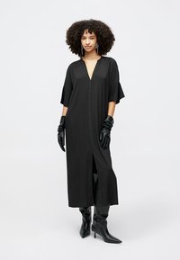 Duga crna haljina s kratkim rukavima, prednjim zatvaračem i bočnim prorezima. Nosivana s crnim rukavicama i čizmama do koljena sa štiklom. Glatka tekstura.