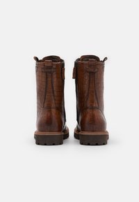 Bottes basses en cuir marron avec une texture crocodile, un languette de tirage arrière et une semelle en caoutchouc robuste avec une bande de roulement visible.