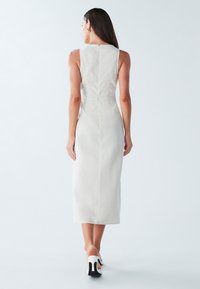 Mouwloze, knielange jurk van lichtbeige linnen met een aansluitende pasvorm, voorzien van een rugrits en subtiele naaddetails.