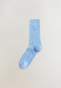 Világoskék pamutzokni bordázott szegéllyel, sima textúrájú, és egy kis logó hímzéssel a boka közelében. Klasszikus kialakítású és formájú.