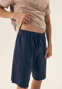 Szorty w nawigacyjne wzory z miękkiego materiału, z elastycznym pasem i sznurkiem. Wzór zdobiony motywem diamentowym na całej powierzchni.