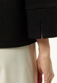 Maglione nero con texture a zig zag, maniche ampie e dettaglio spaccato. Abbinato a una gonna in satin chiara.