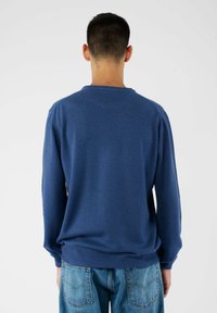 Niebieski sweter dzianinowy z okrągłym dekoltem i długimi rękawami, z prążkowanymi mankietami i dołem. Noszony z jasnymi dżinsami.