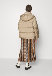 Beige puffjakke med hætte, med en quiltet design. Kombineret med en lang, mønstret nederdel i brune, orange og creme farver. Sorte ankelstøvler.