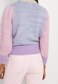 Stickad tröja i en mjuk blandning av ljusblå och rosa, långa texturerade ärmar, ribbat fåll och subtila färgvariationer.