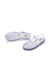 Sandalias claras, en gelatina, con un diseño trenzado en lavanda translúcida. Cuentan con una correa para el tobillo y una suela plana, etiquetadas con "melissa" en la plantilla.