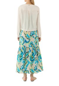 Biała bluzka z długimi rękawami o okrągłym dekolcie, połączona z wielokolorową, warstwową spódnicą maxi z niebieskimi i zielonymi wzorami.
