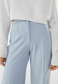 Light blue tailored pants with a smooth texture, side pockets, and clean lines, paired with a cropped white knit sweater featuring ribbed cuffs.