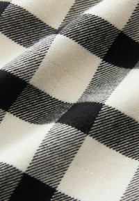 Schwarz-weißer Karostoff mit einer Mischung aus großen Quadraten mit strukturierten Oberflächen, die abwechselnd aus einfarbigen und gemusterten Geweben bestehen.