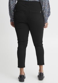 Svarta, åtsittande byxor med en mjuk yta, med två bakfickor med triangulära lock och små dekorativa nitar. Kapad längd vid anklarna.