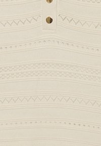 Krémsvětlý pletený top s horizontálními vzory, zdobený knoflíky a strukturovanými pásy. Materiály zahrnují prodyšnou látku s dekorativními detaily.