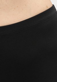 Κοντινό πλάνο φωτεινής επιδερμίδας με φακίδες πάνω από το λαιμό ενός ρούχου από μαύρο υφαντό ύφασμα με ριγέ μοτίβο, που δείχνει τις λεπτομέρειες της ραφής.