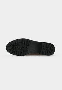 Semelle d’une chaussure marron avec un motif de bande de roulement noir profond conçu pour l'adhérence et la durabilité, présentée sur un fond clair uni.