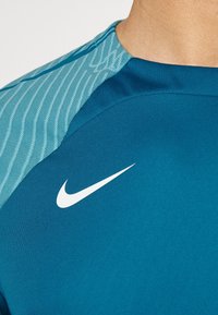 Närbild av en person som bär en blå sporttröja med en vit Nike-swoosh-logga på bröstet och mönstrade ärmar.