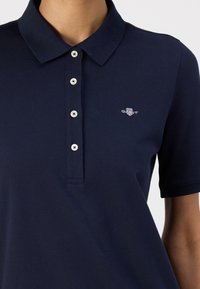 Mornarska polo majica z teksturirano tkanino, trakom z tremi gumbi ter majhnim vezenim logotipom na levem prsnem delu. Kratki rokavi in ribasto ovratnik.