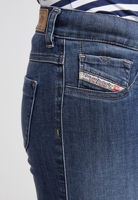 Mörkblå denimjeans med medelhög midja, sidoficka och liten bakficka med en etikett som säger "Diesel Industry."