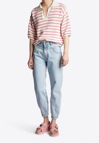 Gestreepte gebreide polo met v-hals in crème en roze, gecombineerd met lichtblauwe tapering jeans en roze sandalen met gespen.