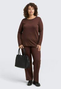 Bruine lange mouwen top en bijpassende broek van ribbeltextuur. Een zwarte handtas met dubbele handvatten en stevige zwarte schoenen maken de outfit compleet.