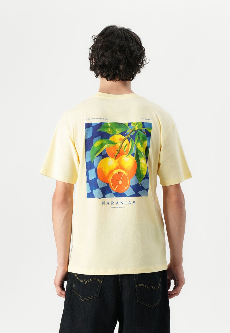 T-shirt di cotone gialla con grafica di frutti arancioni su uno sfondo a check blu. Vestibilità rilassata con maniche corte e scollatura tonda.