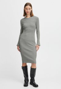 Abito a coste grigio chiaro con scollatura a barca e maniche lunghe, abbinato a stivali neri in pelle modello knee-high con dettagli in metallo.