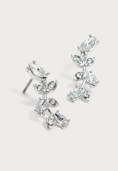 Boucles d'oreilles couleur argent avec des pierres claires taillées en marquise, disposées dans un délicat design de feuilles et de branches sur un fond uni.