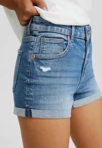 Ljusblå denimshorts med en slitning och uppvikt nederkant. Standard femficksdesign med kopparfärgade detaljer.
