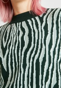 Gestrickter Pullover mit einem Wellenmuster in Grün und Hellblau, einem gerippten Rundhalsausschnitt und weicher Textur.