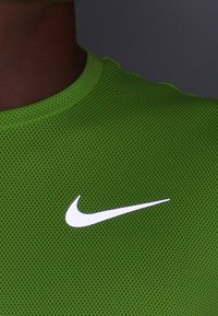 Camiseta deportiva de malla verde con un cuello redondo y un distintivo logo blanco de Nike en la parte frontal, que muestra una textura transpirable.