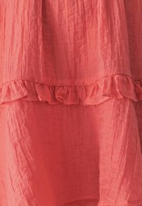 Kleid in Korallenfarbe mit einem gekräuselten Textur und Rüsche am Saum. Der Stoff ist leicht und fließend, mit einem gestuften Design und zarten Falten.