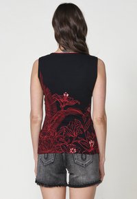 Top senza maniche nero con ricami floreali rossi sulla parte posteriore, abbinato a pantaloni corti in denim grigi. La maglietta ha un collo rotondo e una silhouette aderente.