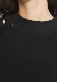 Czarny sweter dzianinowy z wysokim dekoltem, z teksturowymi akcentami na ramionach i detalem z guzikiem przypominającym perłę.