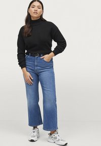 Maglione nero a dolcevita, jeans ampi in denim blu a vita alta e sneakers bianche con accenti neri. Outfit semplice, testurizzato e casual.