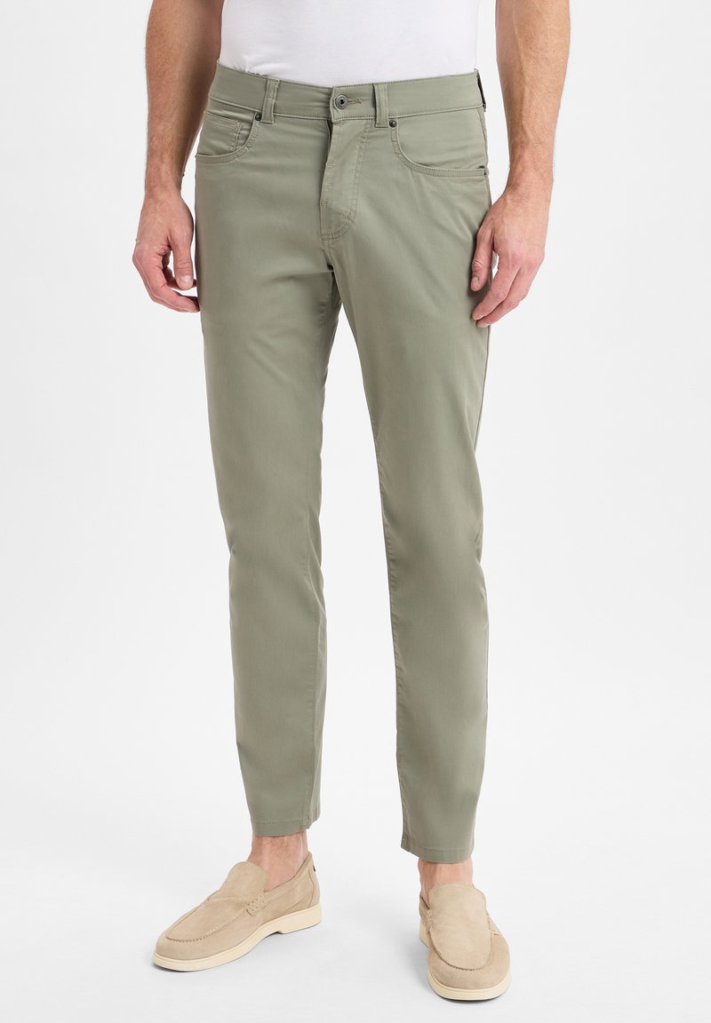 Olivgrüne Slim-Fit-Hose mit glatter Textur, Fronttaschen und Knopfverschluss, kombiniert mit beigen Slippern.