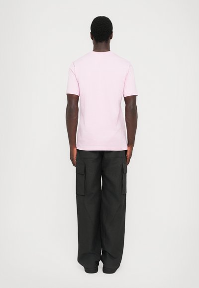Pink bomulds T-shirt med rund hals, parret med sorte cargo bukser med sidelommer og en løs pasform. Set fra ryggen.