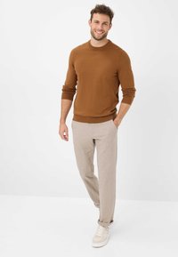 Brun strikket sweater med ribbenmanchetter, parret med lysebeige teksturerede bukser og hvide sneakers, der har en afslappet pasform og sidelommer.
